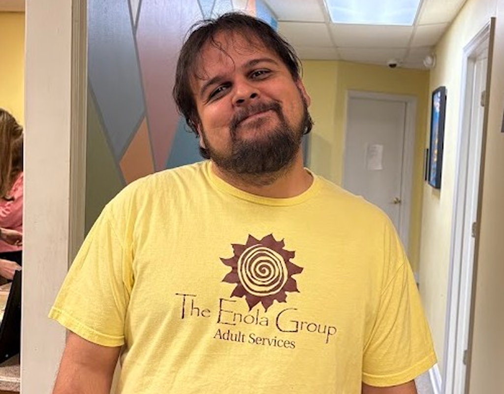 A person smiling wearing The Enola Group Adult Services t-shirt 
